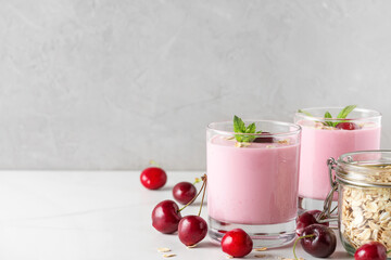 two glasses of healthy cherry yogurt with fresh berries, oats and mint on white marble table. healthy breakfast. close up