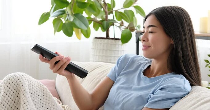 Woman changing channel and watching tv sitting on sofa at home