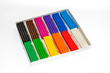 Multi-colored plasticine sticks in a cardboard box. Colorful plastic polymer clay set on white background.