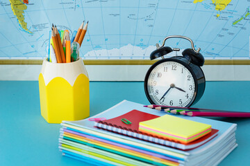 black clocks, pens, pencils, notebooks on map background. Back to school concept. Beginning of school year. Copy space for text.