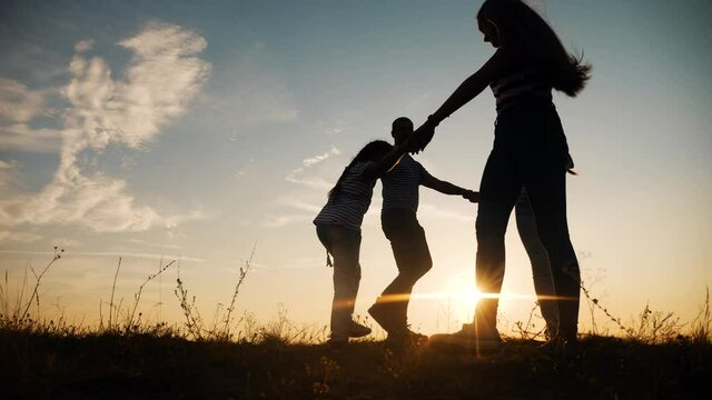 happy family mom dad and daughter play round dance silhouette at sunset. people in park kid dream concept. happy family parents with little kid child daughter play in park on grass fun holding hands