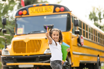 Cute girl with a backpack standing near bus going to school posing to camera pensive close-up