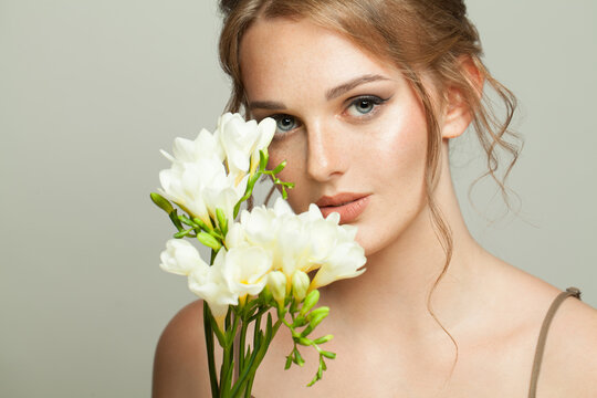 Healthy woman with natural clear skin with freckles holding white flowers