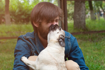 Man with his dog playing outdoor in the park. Young owner hugs his pet, dog lick nose her owner