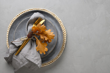 Elegant table setting with autumn oak leaves and golden cutlery on grey background. Flat lay, top...