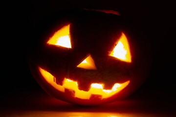 scary pumpkin face for halloween in a dark room candle burns inside for holiday decor, postcards and premises