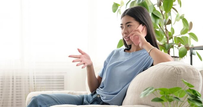 Happy korean woman talking on mobile phone at home