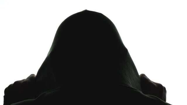 A person in silhouette puts a hood over their head.  View from behind, with bright white background.