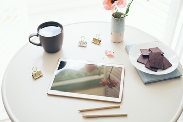 Online education at home concept. Top view of the  white color table with tablet, cup of tea and  chocolate on it. Lifestyle photo, natural light