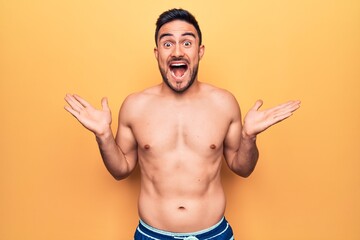 Fototapeta premium Young handsome man with beard wearing sleeveless t-shirt standing over yellow background celebrating victory with happy smile and winner expression with raised hands