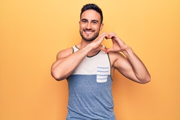 Young handsome man with beard wearing sleeveless t-shirt standing over yellow background smiling in...