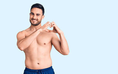 Young handsome man wearing swimwear smiling in love showing heart symbol and shape with hands. romantic concept.