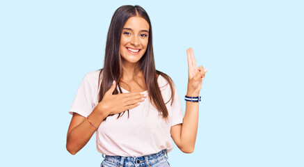 Young hispanic woman wearing casual white tshirt smiling swearing with hand on chest and fingers up, making a loyalty promise oath