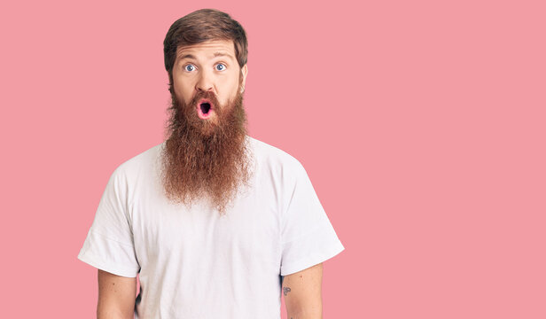Handsome young red head man with long beard wearing casual white tshirt afraid and shocked with surprise expression, fear and excited face.