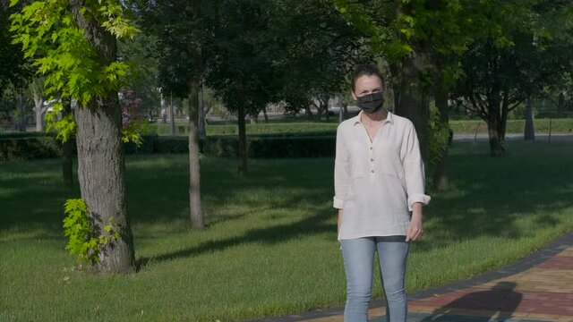 Quarantine concept. A woman walks in the park in a protective mask.