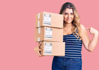 Young caucasian woman holding delivery package pointing finger to one self smiling happy and proud