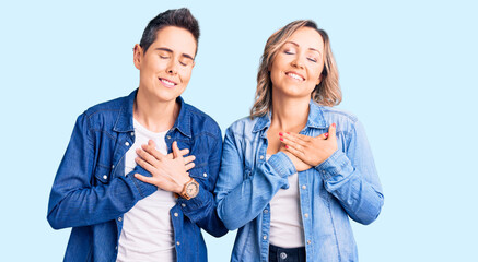 Couple of women wearing casual clothes smiling with hands on chest with closed eyes and grateful gesture on face. health concept.