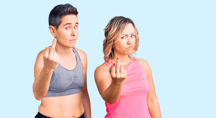 Couple of women wearing sportswear showing middle finger, impolite and rude fuck off expression