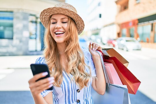 Young beautiful shopper woman smiling happy going to the shops sales holding shopping bags ourtdoors, smiling happy using smartphone