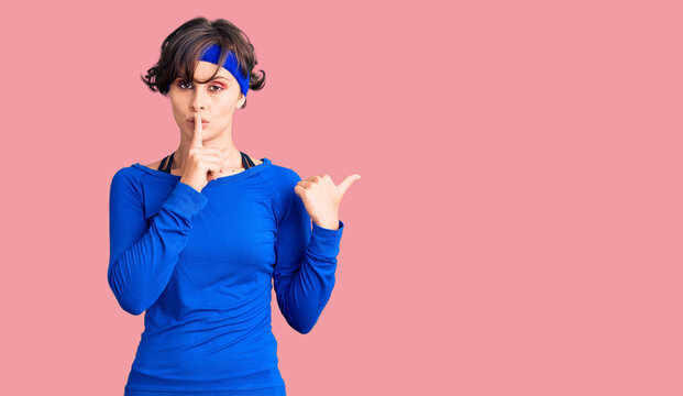 Beautiful young woman with short hair wearing training workout clothes asking to be quiet with finger on lips pointing with hand to the side. silence and secret concept.