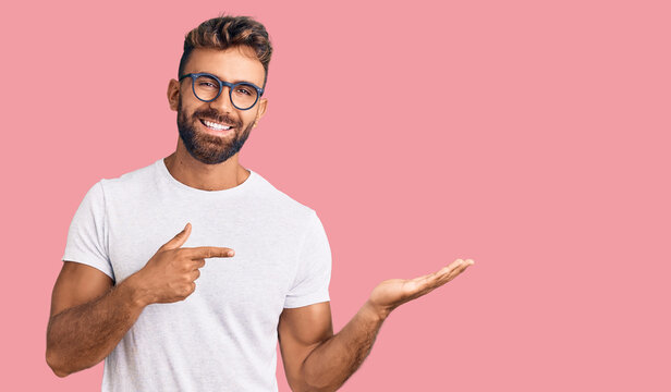 Young hispanic man wearing casual clothes and glasses amazed and smiling to the camera while presenting with hand and pointing with finger.