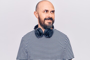 Young handsome man listening to music using headphones looking to side, relax profile pose with natural face and confident smile.