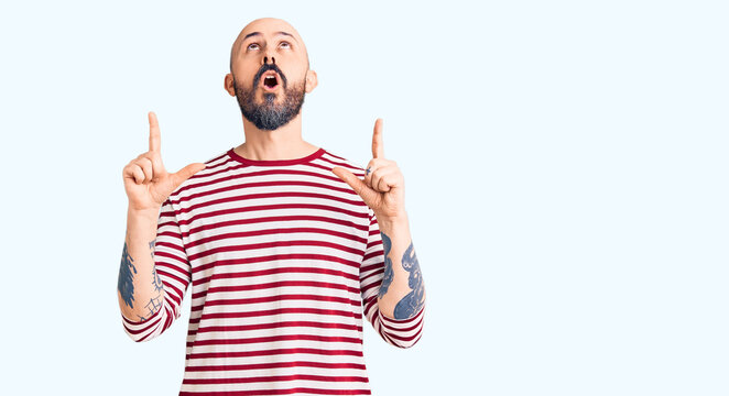 Young handsome man wearing casual clothes amazed and surprised looking up and pointing with fingers and raised arms.
