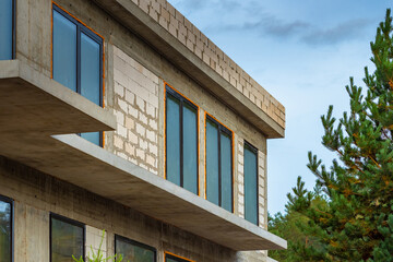 A foam block house is being built. A house under construction near the pines. Construction of cottages on individual projects. A fragment of a stone building under construction.