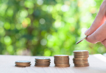 stack of coins and hand with coin on the nature blurred background with bokeh lights