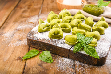 Tortellini e tortelloni typical dishes emilia italy. Food background with homemade raw Italian tortelloni and ingredients for green pesto on wooden background . High angle view. Copy space.