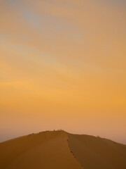 People climbing a dune in a desert during amazing sunset golden hour, in Huacachina desert, Ica, Peru