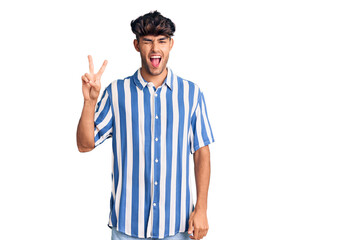 Young hispanic man wearing casual clothes smiling with happy face winking at the camera doing victory sign with fingers. number two.