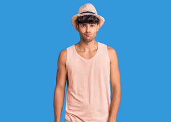 Young hispanic man wearing summer hat puffing cheeks with funny face. mouth inflated with air, crazy expression.
