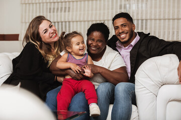 three generations with grandfather, daughter, husband and granddaughter, sitting and smiling on the living room sofa