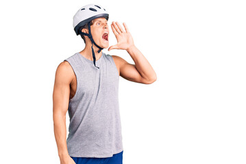 Young handsome man wearing bike helmet shouting and screaming loud to side with hand on mouth. communication concept.