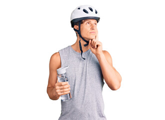 Young handsome man wearing bike helmet holding bottle of water serious face thinking about question with hand on chin, thoughtful about confusing idea