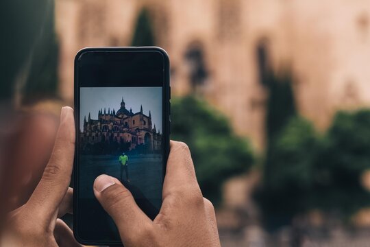 use your mobile phone to take a picture of a boy with the cathedral of Segovia in Spain as a background