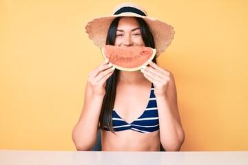 Young beautiful caucasian woman wearing bikini and hat holding slice of watermelon looking positive and happy standing and smiling with a confident smile showing teeth