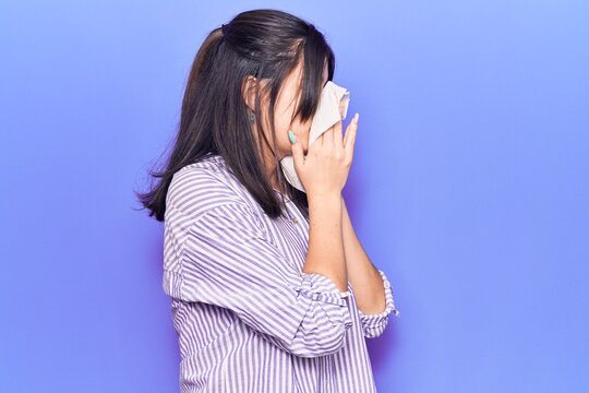 Young hispanic woman illness using paper handkerchief on nose. Standing over isoltated purple background