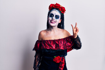 Young woman wearing mexican day of the dead makeup showing and pointing up with fingers number two...