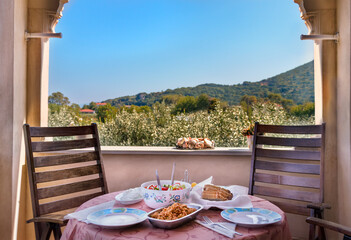 A Greek traditional lunch served on a wooden table at home with a view with olives trees, outdoors.