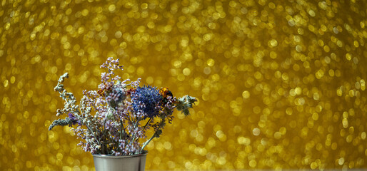 Dry flowers in metal vase on blurred yellow background