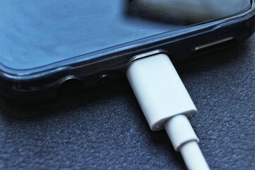 Close-up of a USB type-c connector in a smartphone and an inserted wire. Fast charging. Black discharged phone on black background