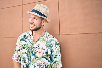 Handsome caucasian man wearing summer hat and flowers shirt smiling happy outdoors