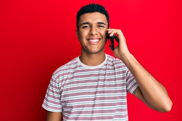 Young arab man having conversation talking on the smartphone looking positive and happy standing and smiling with a confident smile showing teeth