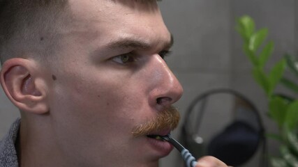 Young caucasian man is brushing teeth with toothbrush in modern bathroom in the morning. Male brushes his teeth with toothpaste, doing morning oral anti cavity hygienic routine