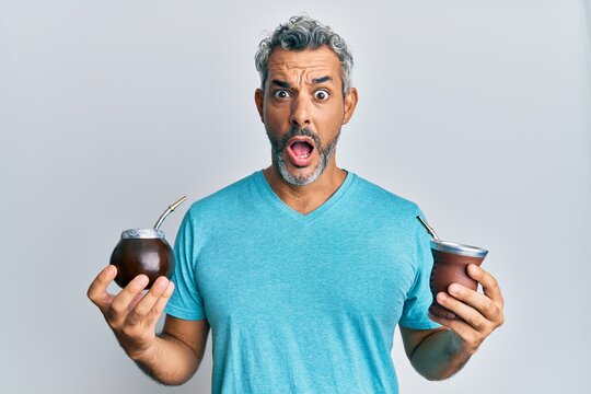Middle age grey-haired man drinking mate infusion afraid and shocked with surprise and amazed expression, fear and excited face.