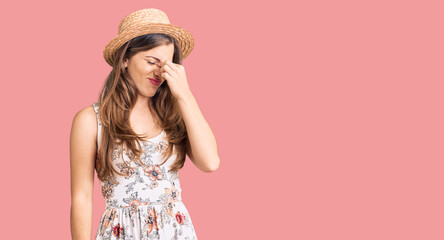 Beautiful caucasian young woman wearing summer hat tired rubbing nose and eyes feeling fatigue and headache. stress and frustration concept.