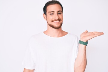 Young handsome man wearing casual white tshirt smiling cheerful presenting and pointing with palm of hand looking at the camera.