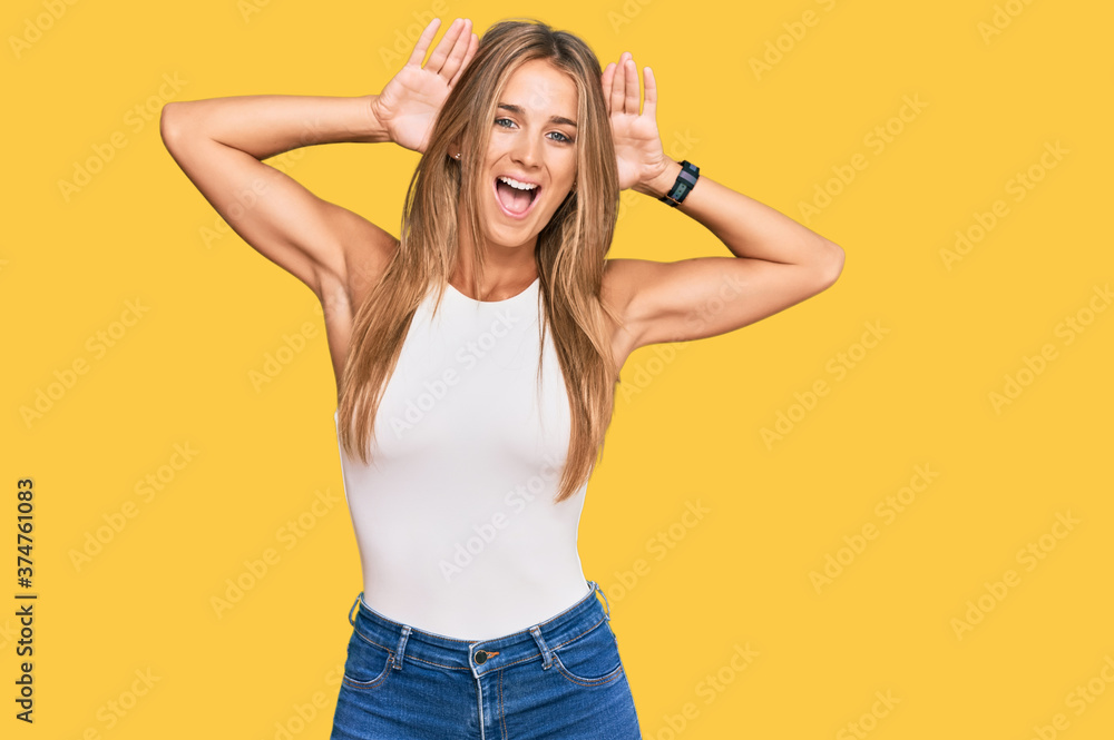 Wall mural Young blonde woman wearing casual style with sleeveless shirt smiling cheerful playing peek a boo with hands showing face. surprised and exited - Wall murals